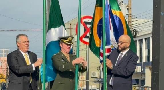 Cerimônia de hasteamento de bandeiras em Ponta Porã, com um oficial militar e dois homens de terno segurando as hastes das bandeiras de Mato Grosso do Sul e do Brasil, em uma edição anterior do 7 de Setembro