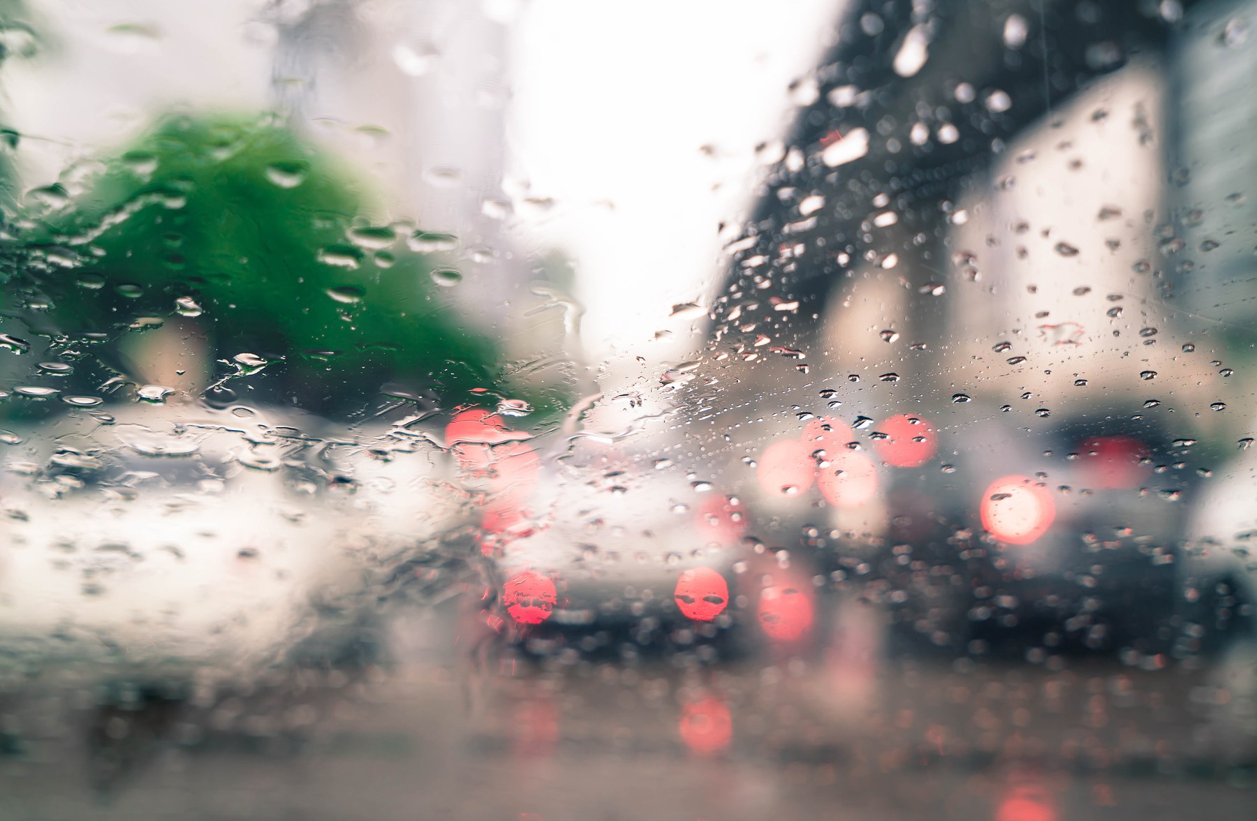 Lluvia fuerte sobre el tránsito, vista desde adentro de un auto, con las luces de freno desenfocadas por el agua en el vidrio