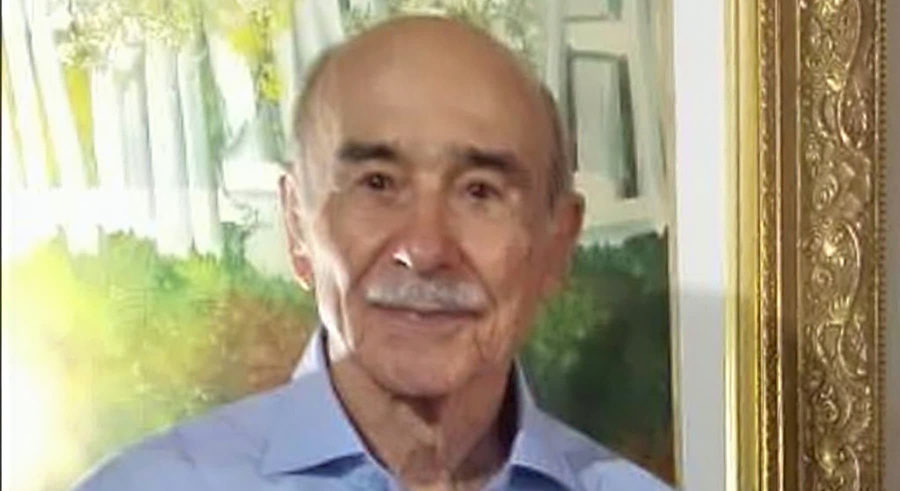 Retrato do médico Astúrio Marques, de camisa azul-clara, diante de um quadro
