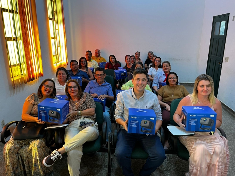 Diretores de escolas sentados no auditório da prefeitura de Bela Vista, cada um segurando a caixa de um projetor