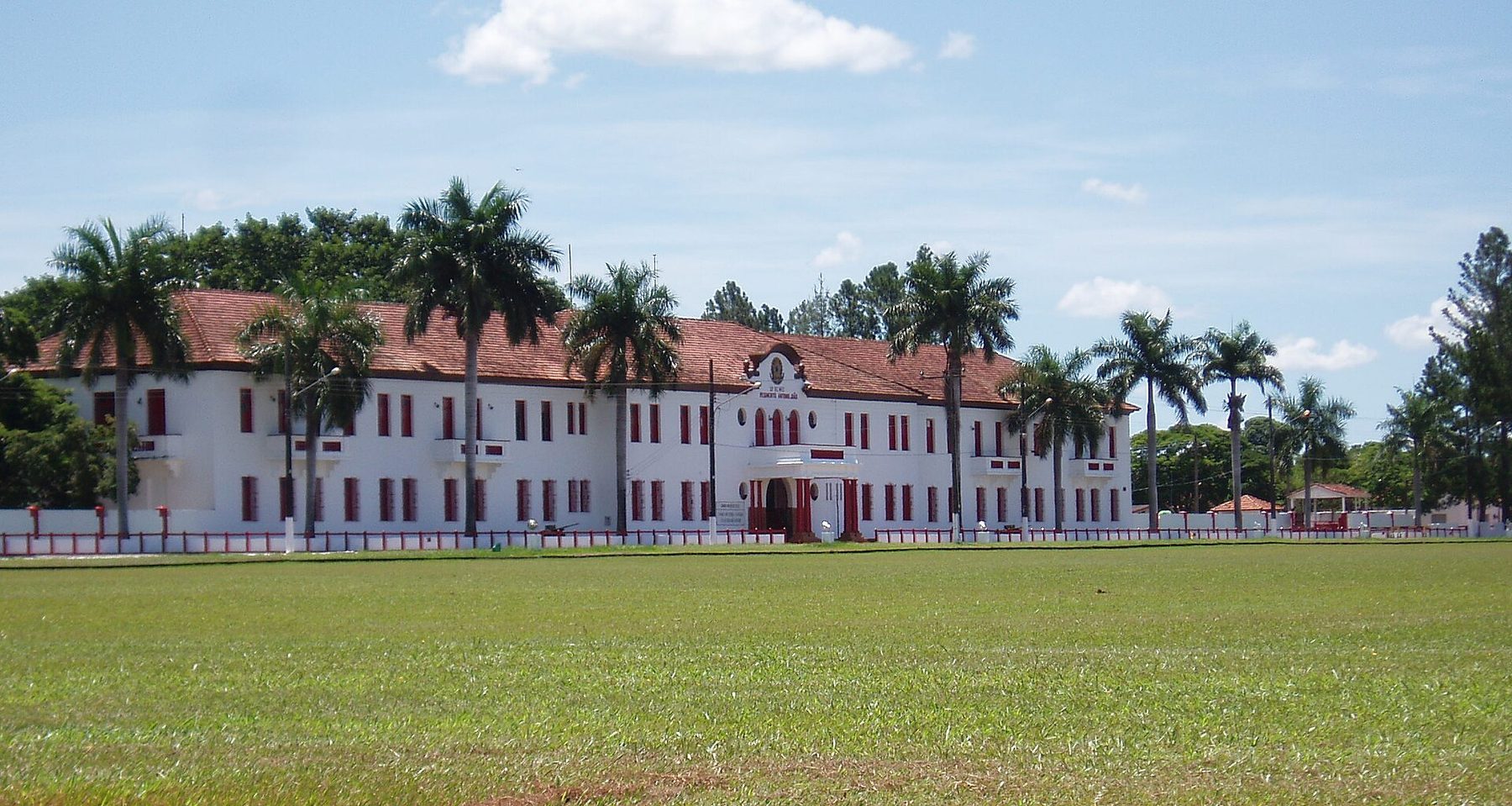 Prédio branco de dois andares com janelas vermelhas e palmeiras na frente, sede do quartel do Exército em Bela Vista, atrás de um gramado