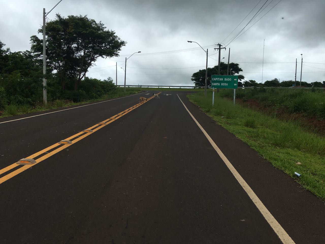 Estrada asfaltada com faixa amarela dupla e placa verde indicando Capitán Bado e Santa Rosa, no acesso a Karapaí