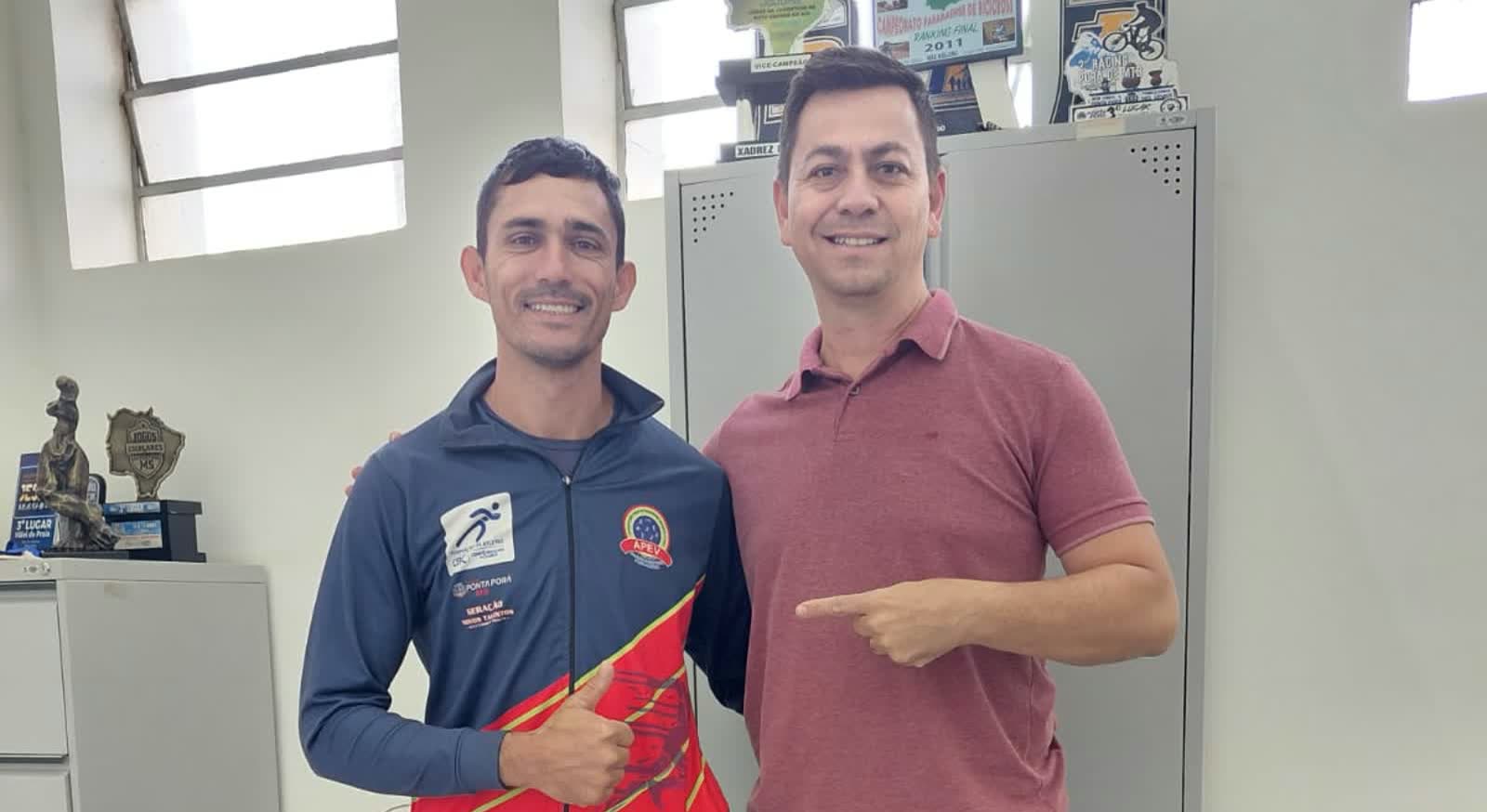 O treinador Fredy Miranda, de agasalho da APEV, ao lado do secretário de Esporte e Lazer Ricardo Torraca, numa sala com troféus ao fundo