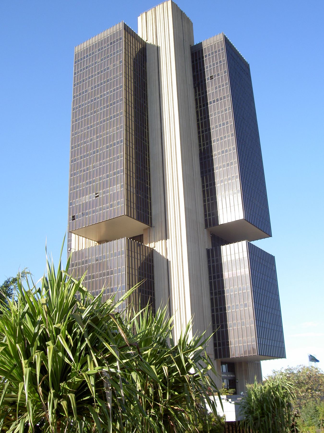 Edificio sede del Banco Central, en Brasilia, de fachada oscura y espejada, visto desde abajo con plantas en primer plano