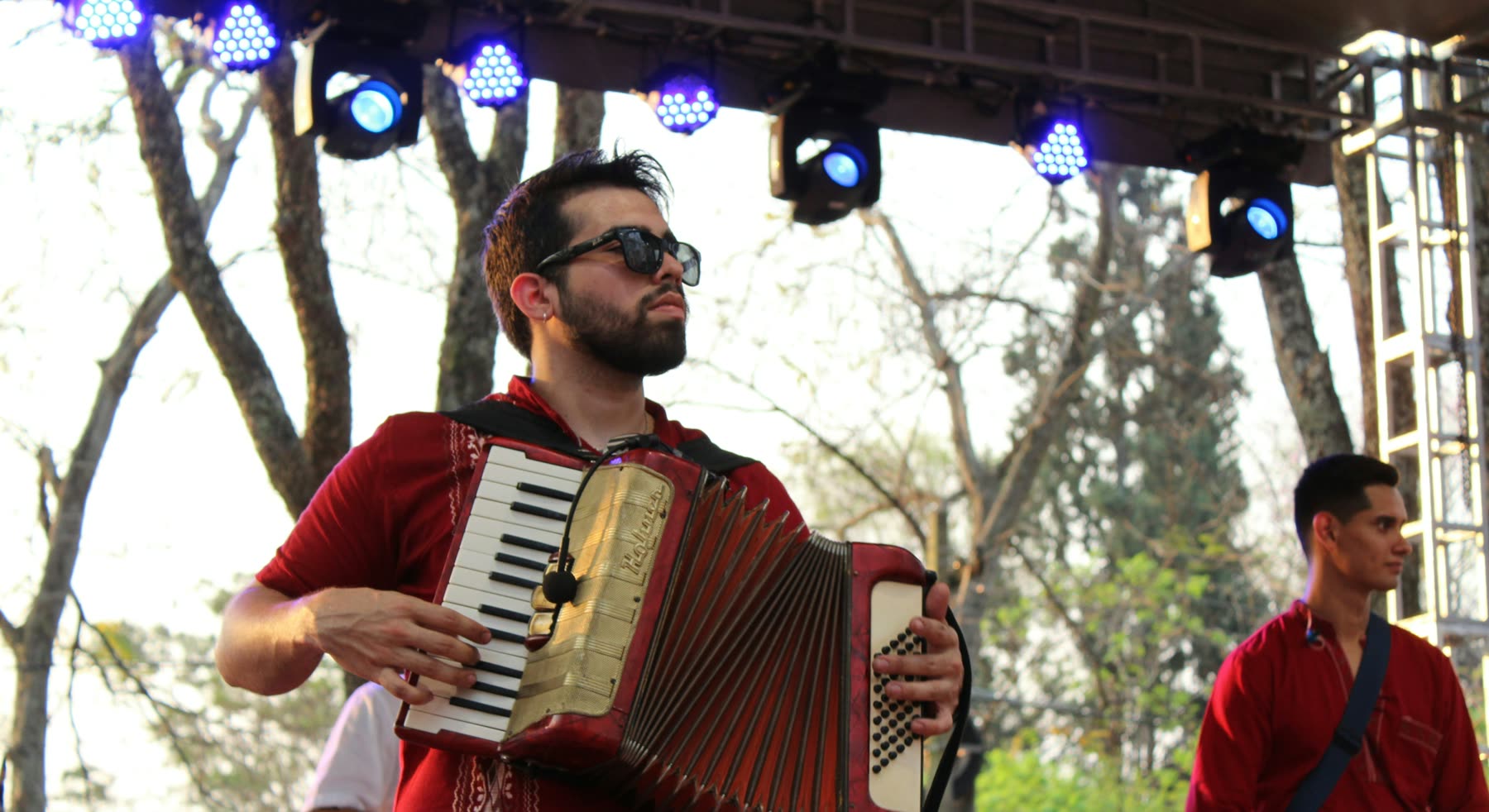 Acordeonista de camisa roja toca en un escenario al aire libre, bajo reflectores