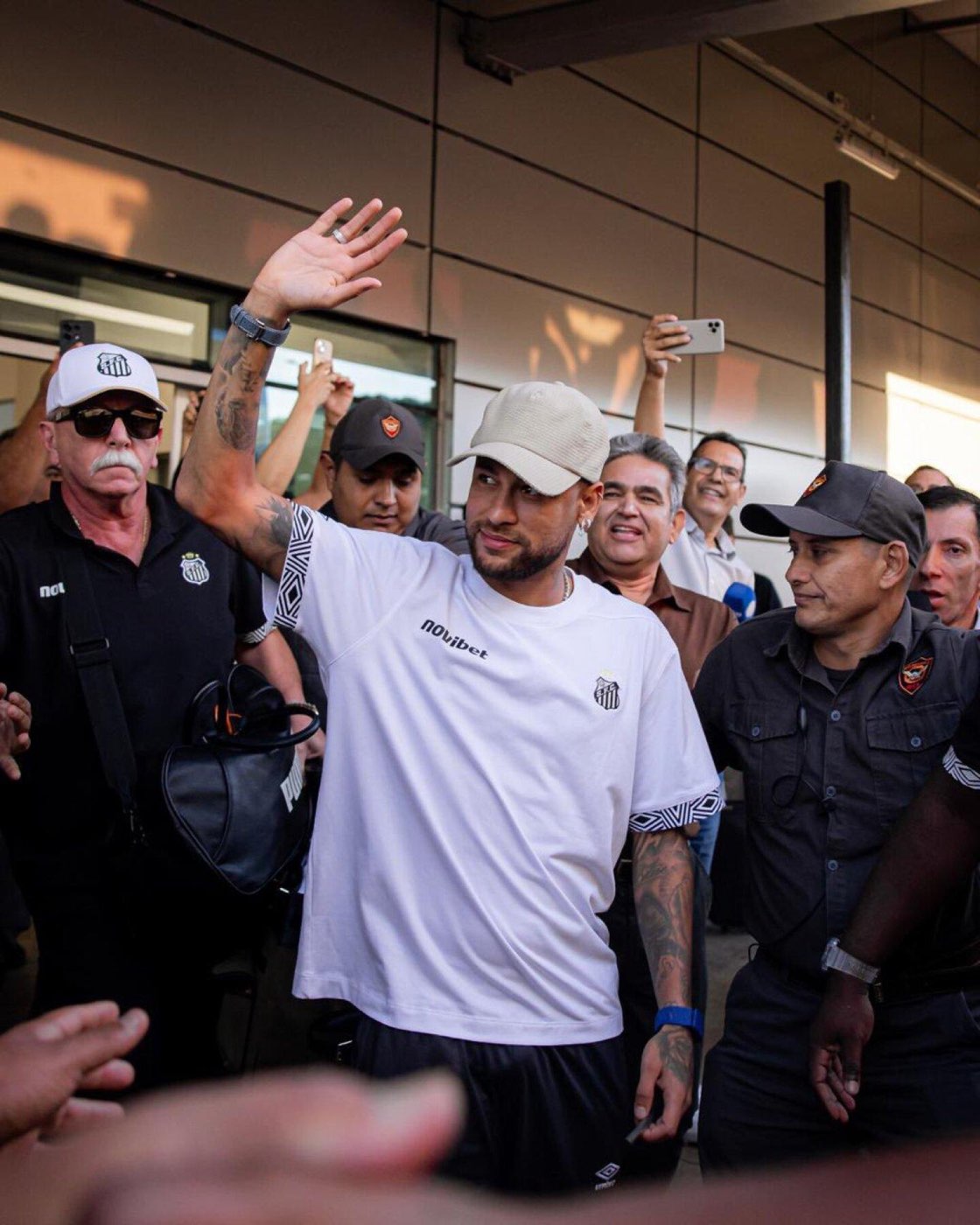 Neymar acena para torcedores cercado de seguranças, num desembarque