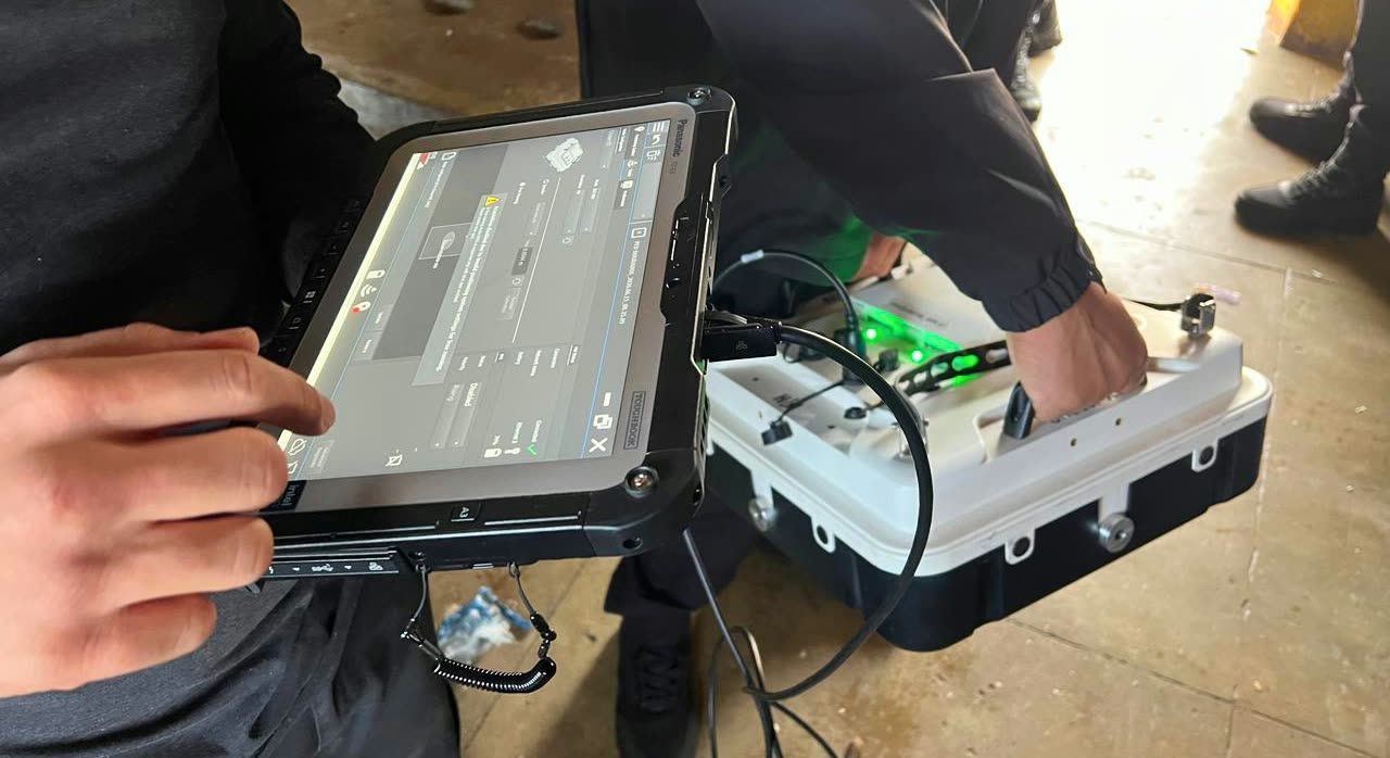 Agente sostiene una tableta conectada por cable a un equipo de escaneo con luces verdes, usado en el operativo dentro de la penitenciaría