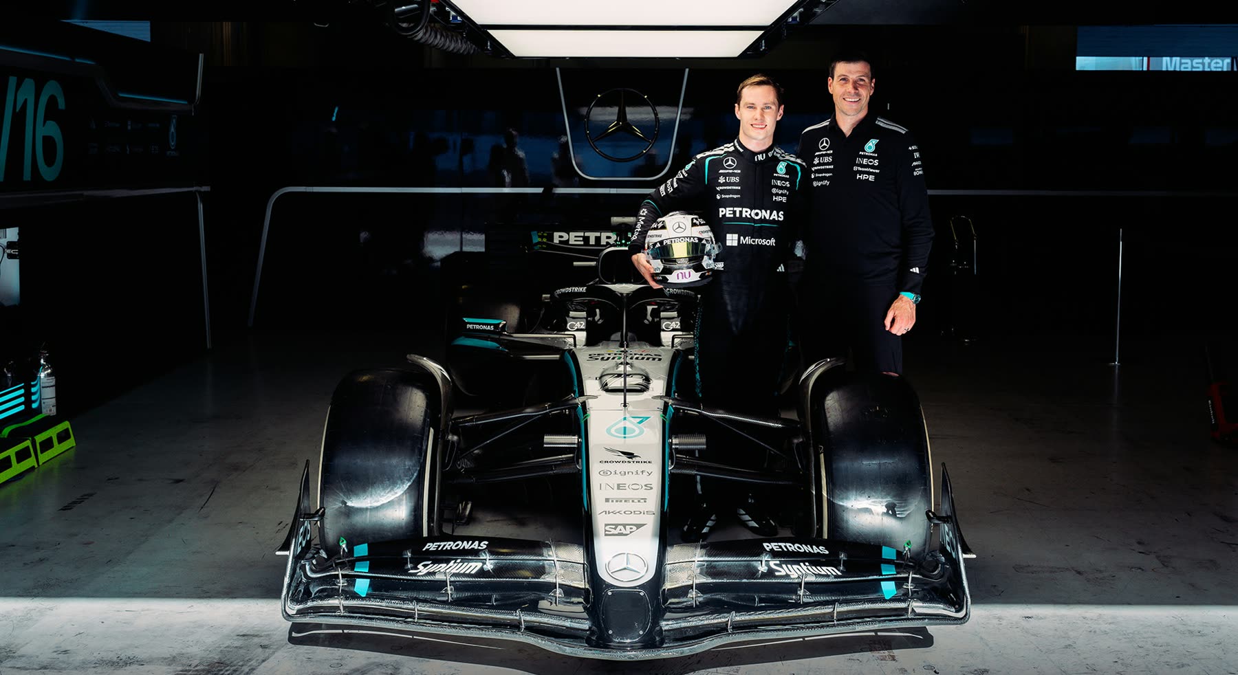 Joshua Duerksen con el casco en las manos junto a un directivo de Mercedes-AMG F1, ambos frente al auto del equipo en el box de Portimão