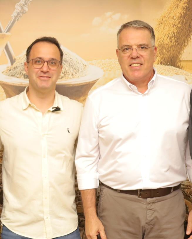 Eduardo Campos e Daniel Kayatt posam lado a lado, de camisa clara, diante de um painel com grãos