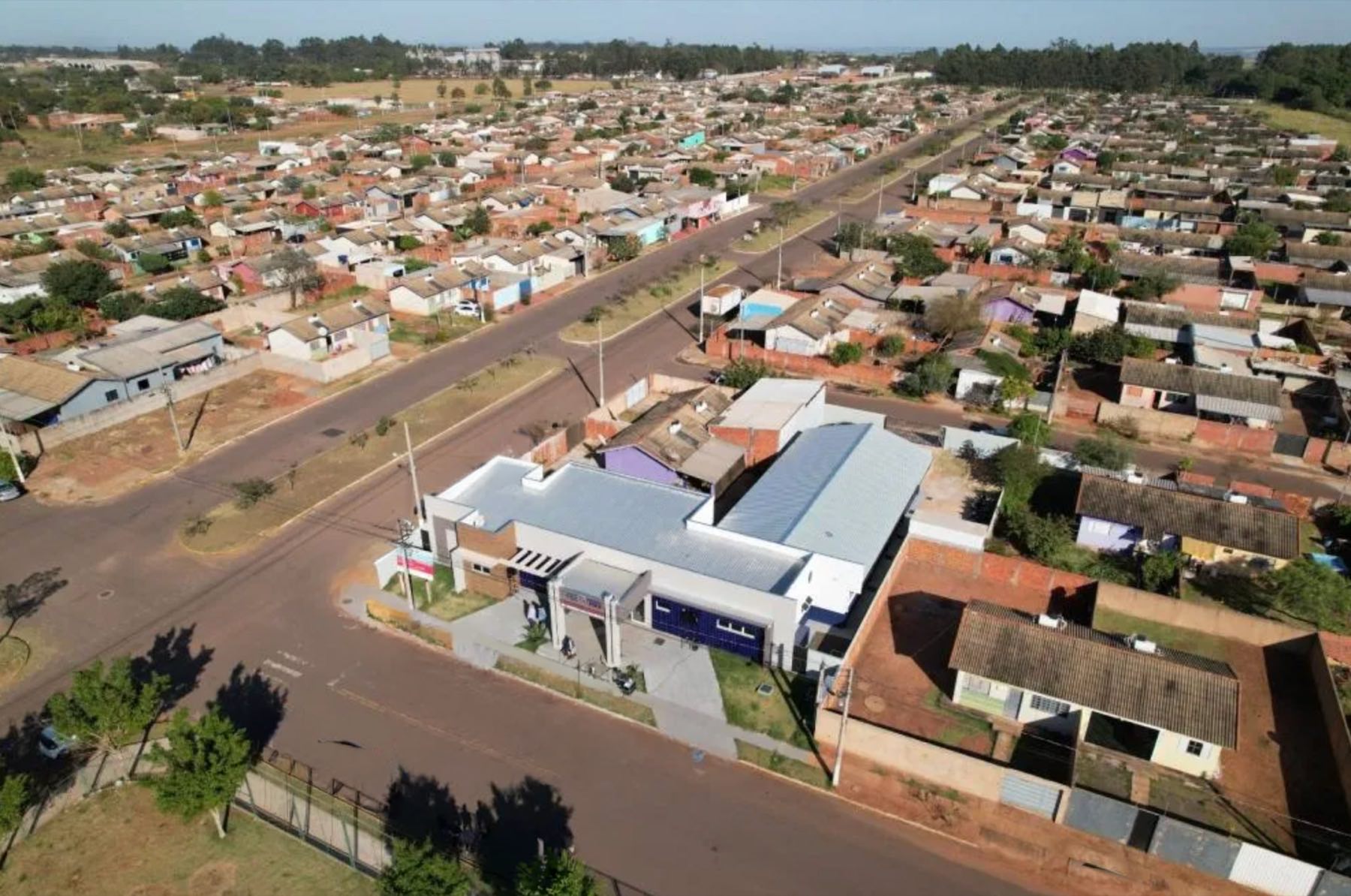Vista aérea do bairro Kamel Saad, com ruas retas, casas de telhado claro e um prédio público de fachada azul e branca
