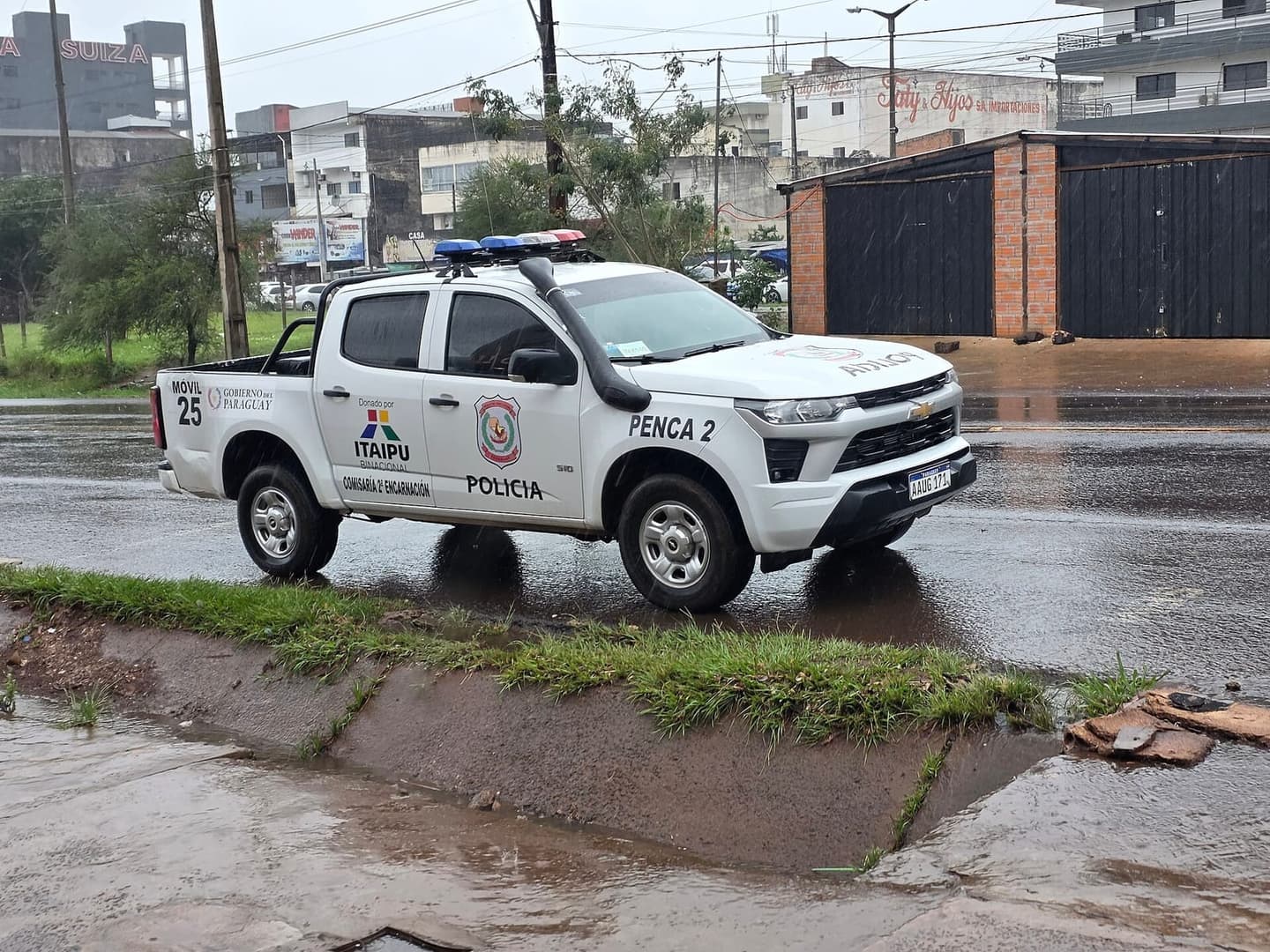 Camionete branca da Polícia Nacional do Paraguai estacionada numa rua molhada de chuva, com sinalizador no teto e o escudo da polícia na porta