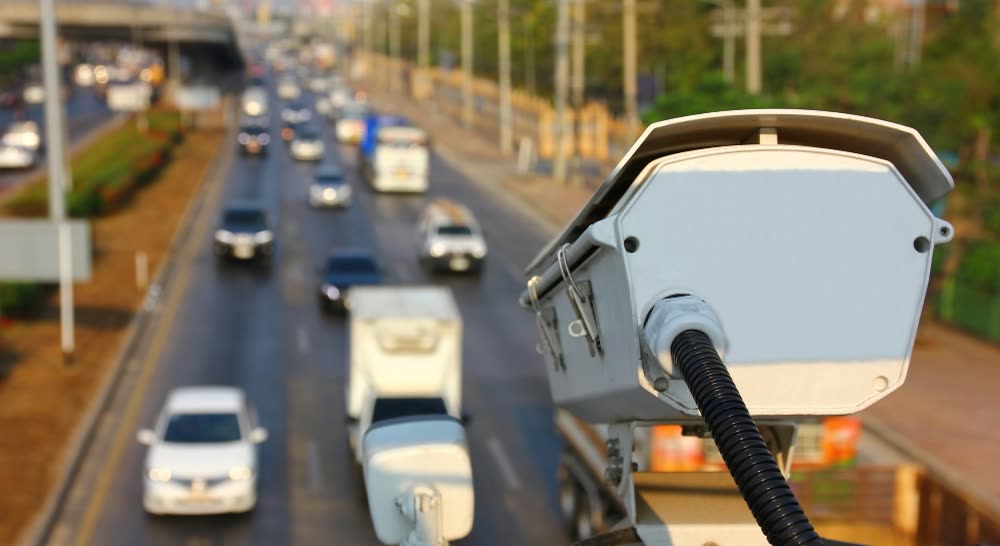 Radar de velocidade montado acima de uma rodovia de pista dupla, com o trânsito desfocado ao fundo