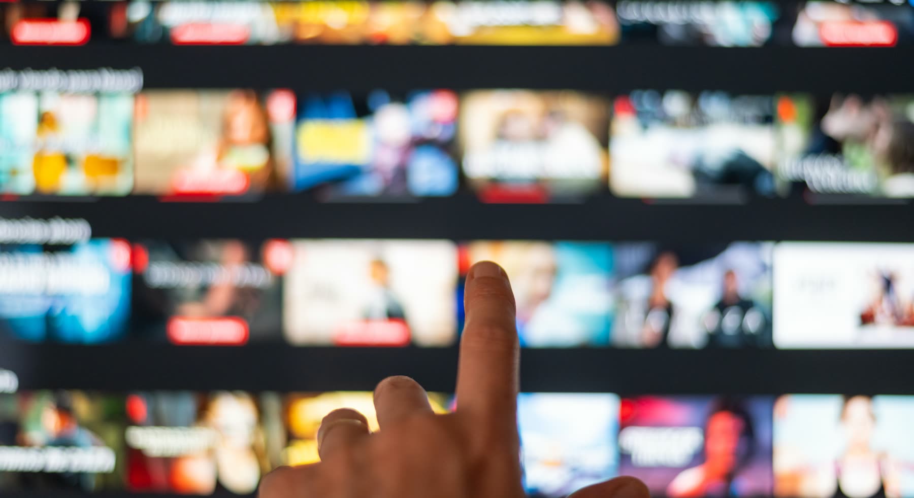 Dedo aponta para a tela de uma televisão com uma grade de programas
