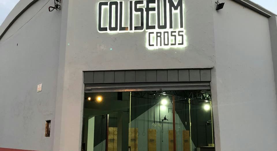 Galpón blanco con las letras Coliseum Cross sobre el portón abierto, dejando ver el salón de entrenamiento al fondo