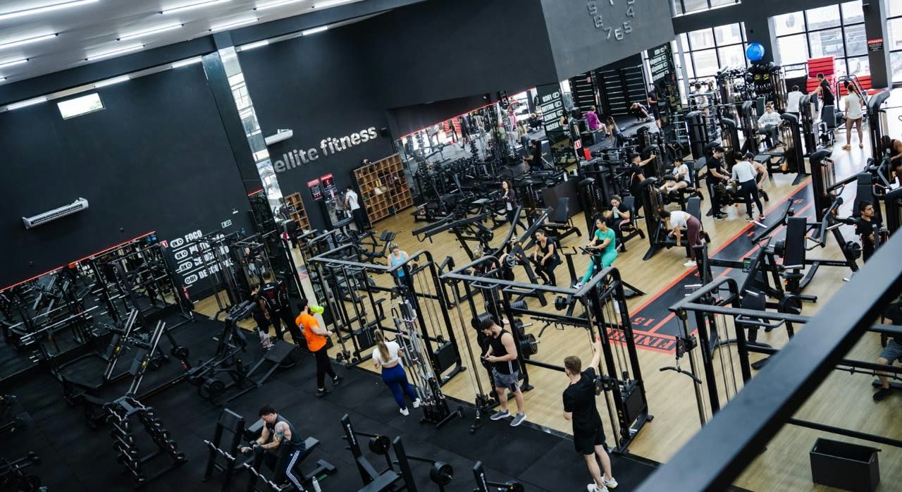 Vista desde arriba del salón de musculación lleno de aparatos, con personas entrenando y el nombre Ellite Fitness en la pared
