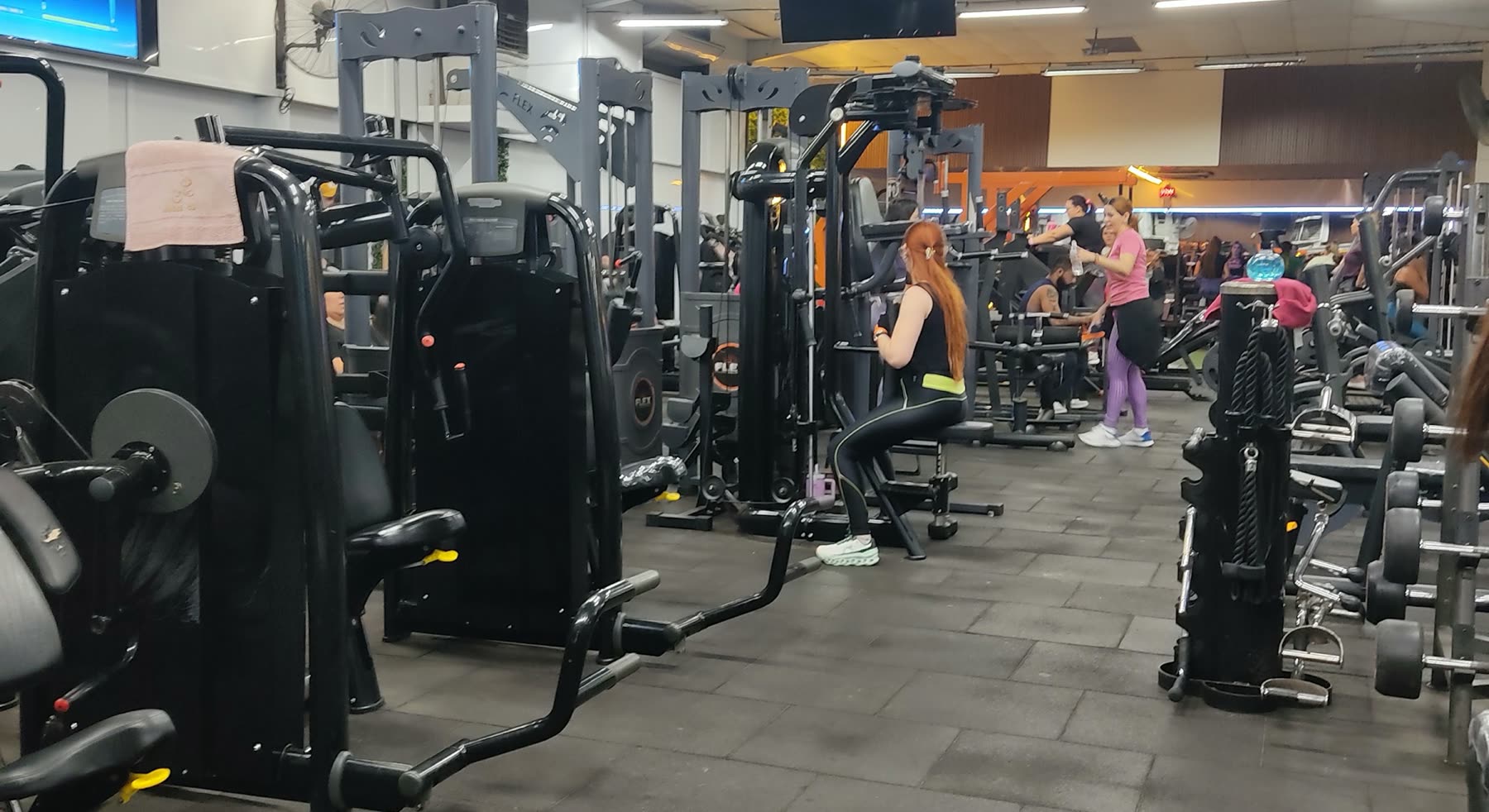 Pasillo de aparatos de musculación con personas entrenando al fondo