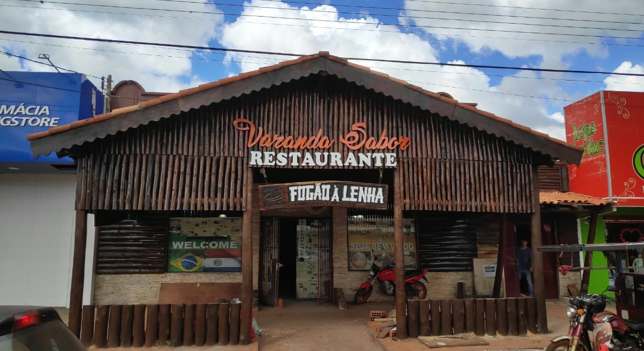 Fachada de madera con el letrero Varanda Sabor Restaurante y el cartel Fogão a Lenha, con motos estacionadas al costado