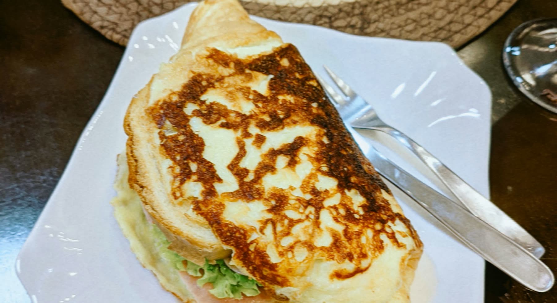 Sándwich de pan de molde tostado con queso derretido, servido en plato cuadrado con tenedor y cuchillo