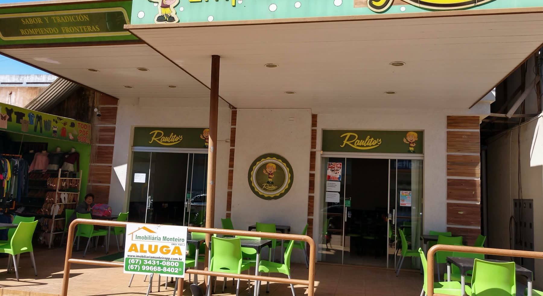 Fachada verde con el nombre Raulitos, mesas y sillas plásticas verdes en la vereda y un cartel de inmobiliaria colgado