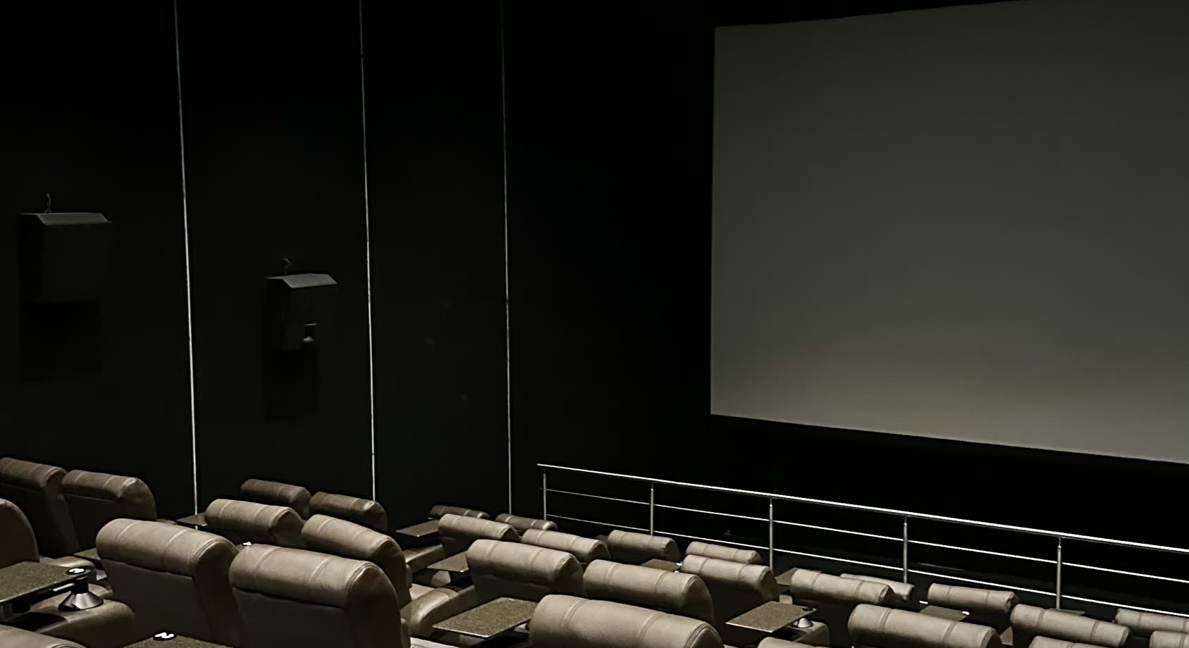 Sala de cine vacía y oscura, con butacas reclinables frente a la pantalla blanca