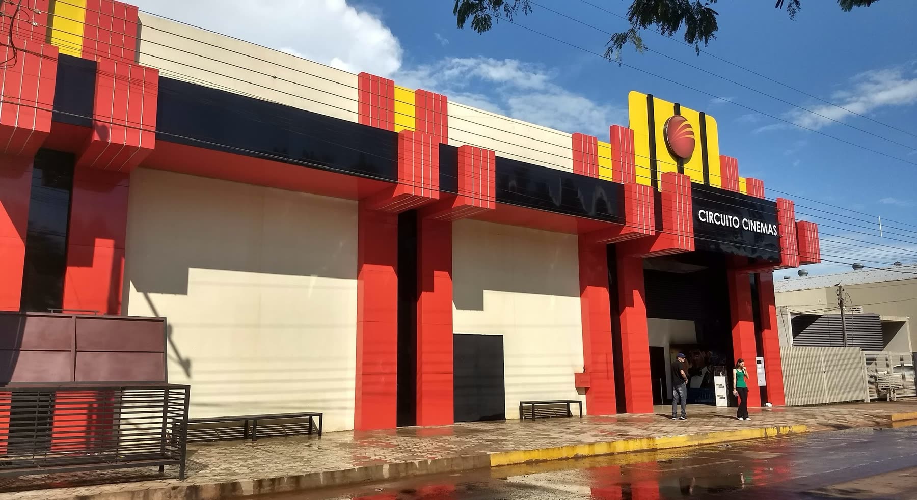 Fachada roja, amarilla y negra del Circuito Cinemas, con personas en la entrada y la vereda mojada