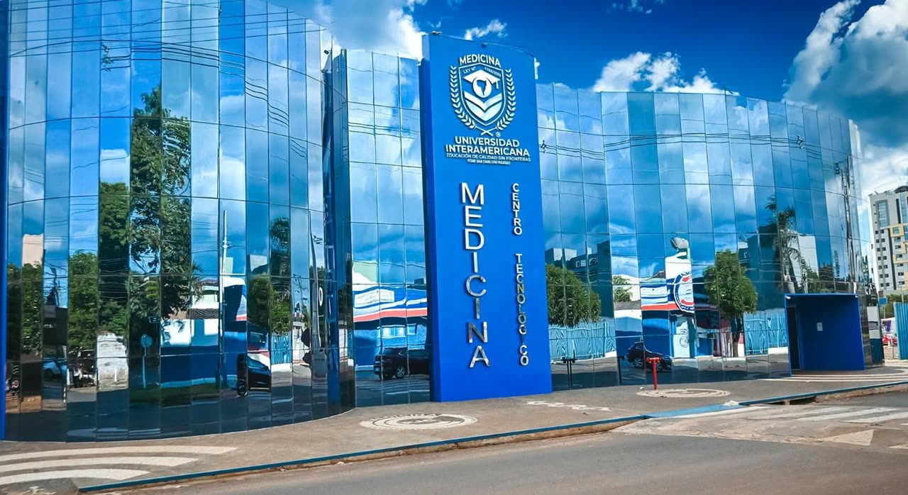 Edificio de vidrio espejado azul con la palabra Medicina escrita en vertical y el escudo de la Universidad Interamericana en la fachada