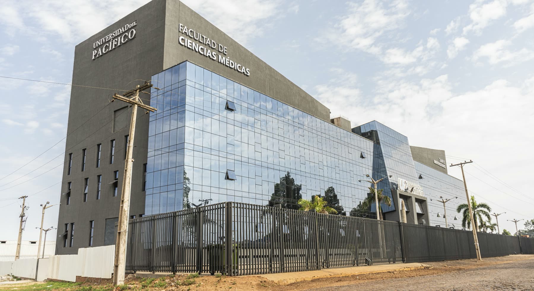 Edificio oscuro de fachada vidriada con la leyenda Universidad del Pacífico y Facultad de Ciencias Médicas, detrás de una reja de hierro