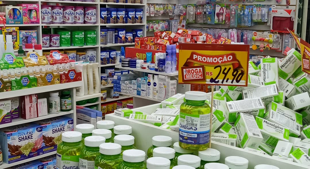 Corredor de farmácia com prateleiras de suplementos e leite em pó e um cartaz vermelho de promoção a 24,90