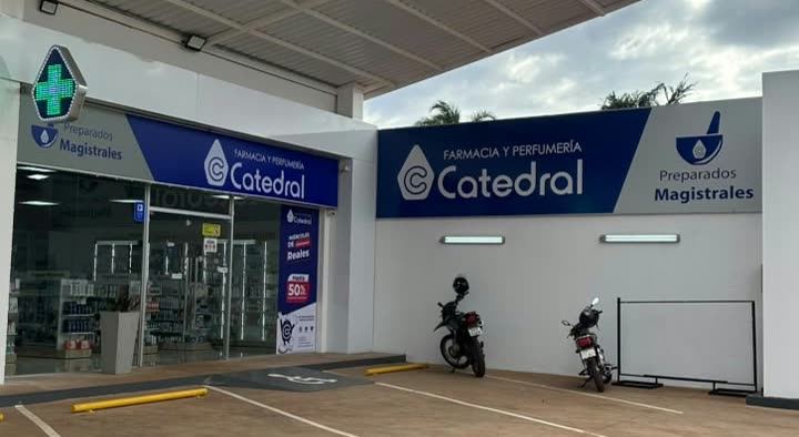 Fachada azul e branca com o letreiro Farmacia y Perfumería Catedral e o aviso de preparados magistrais, com duas motos estacionadas em frente