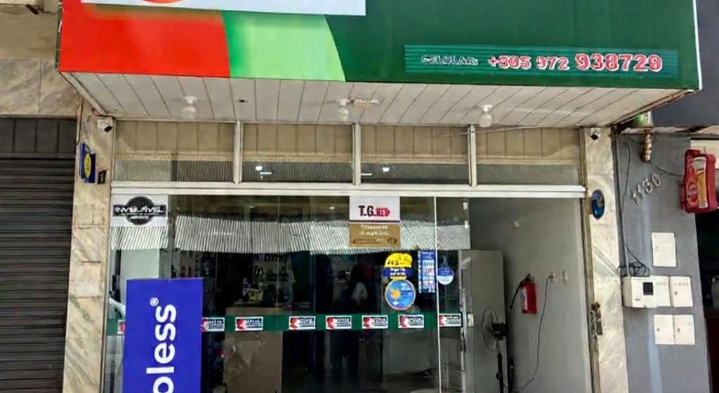 Loja estreita de portas de vidro sob um toldo listrado nas cores da bandeira paraguaia, com um número de celular na placa verde acima