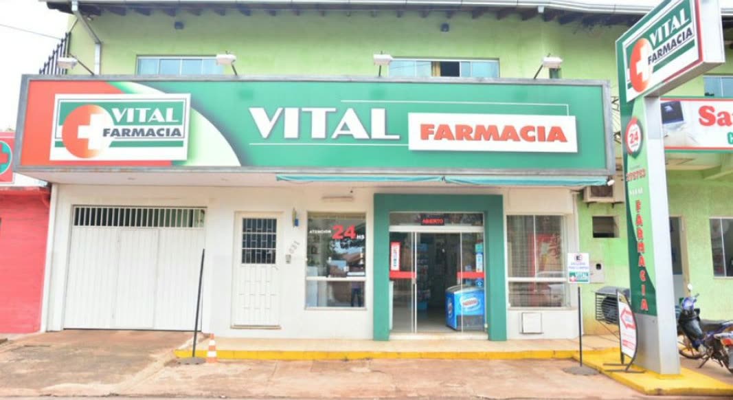 Prédio verde e branco com os letreiros Vital Farmacia sobre a entrada e uma moto estacionada na calçada