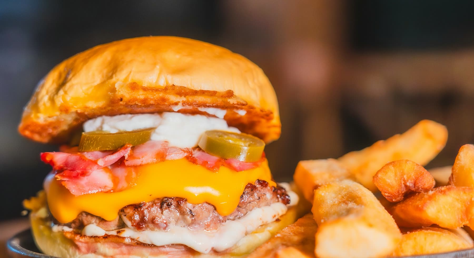Hamburguesa con queso cheddar, panceta, jalapeños y mayonesa junto a una porción de papas rústicas