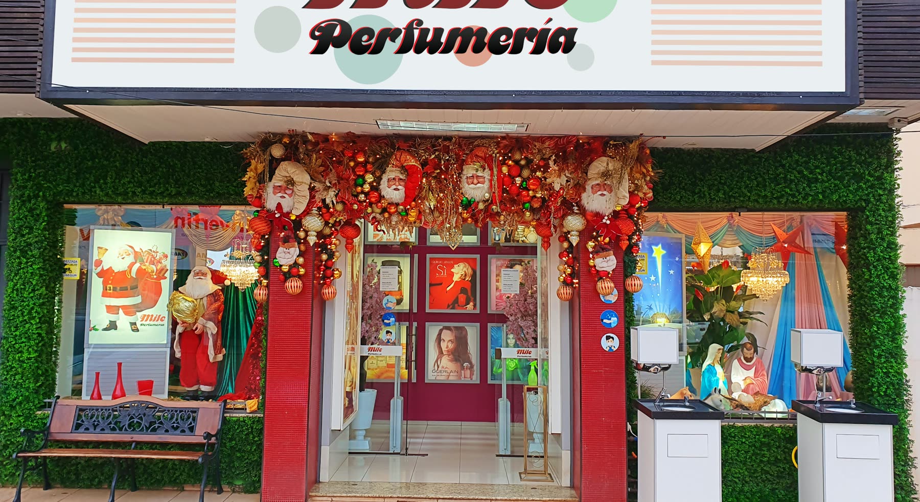 Entrada de perfumería con paredes de follaje artificial y decoración navideña, con guirnaldas, bolas y muñecos de Papá Noel en las vidrieras