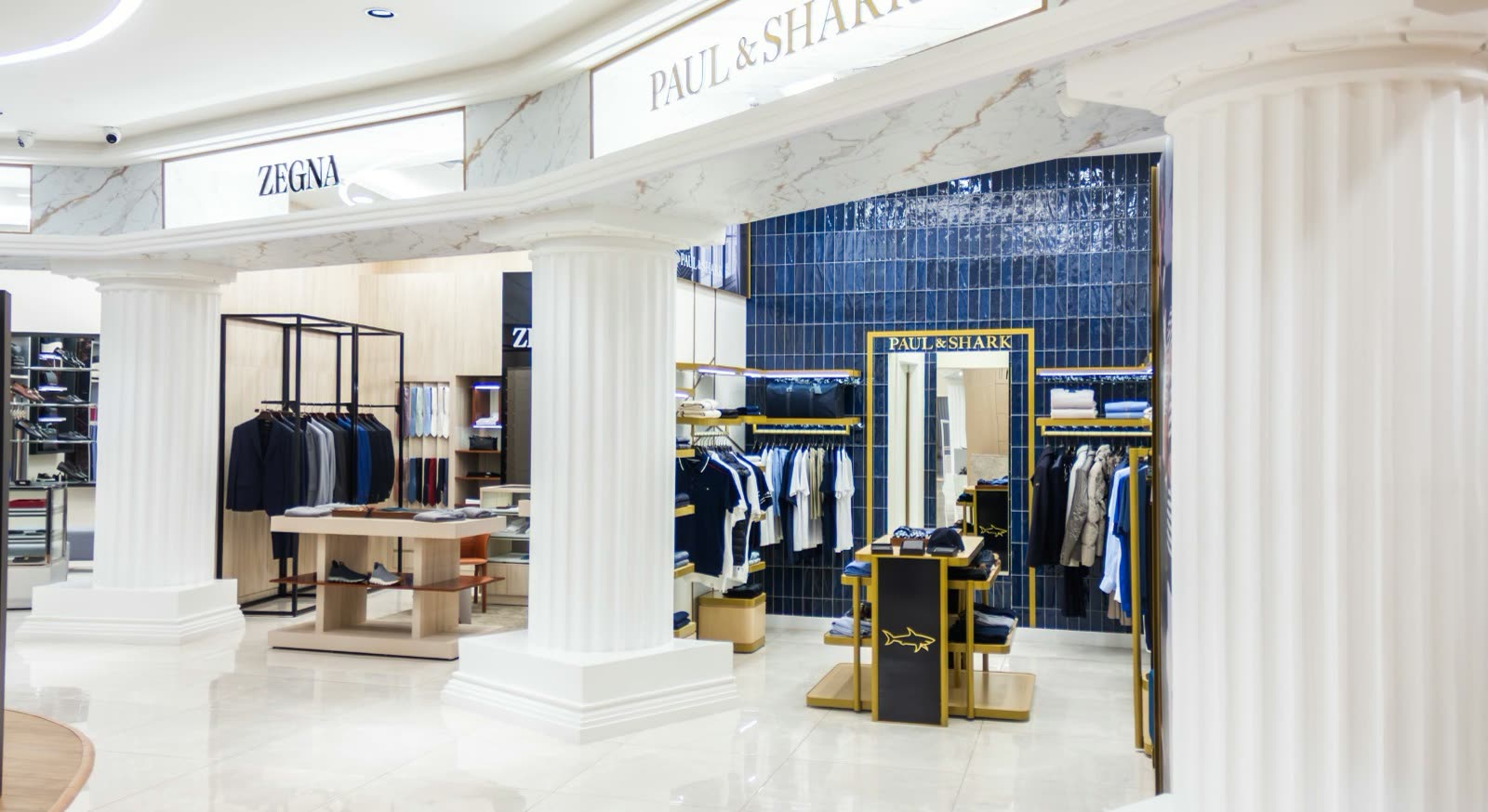 Pasillo de shopping con piso de mármol y columnas blancas, entre los locales Zegna y Paul & Shark con percheros de ropa masculina