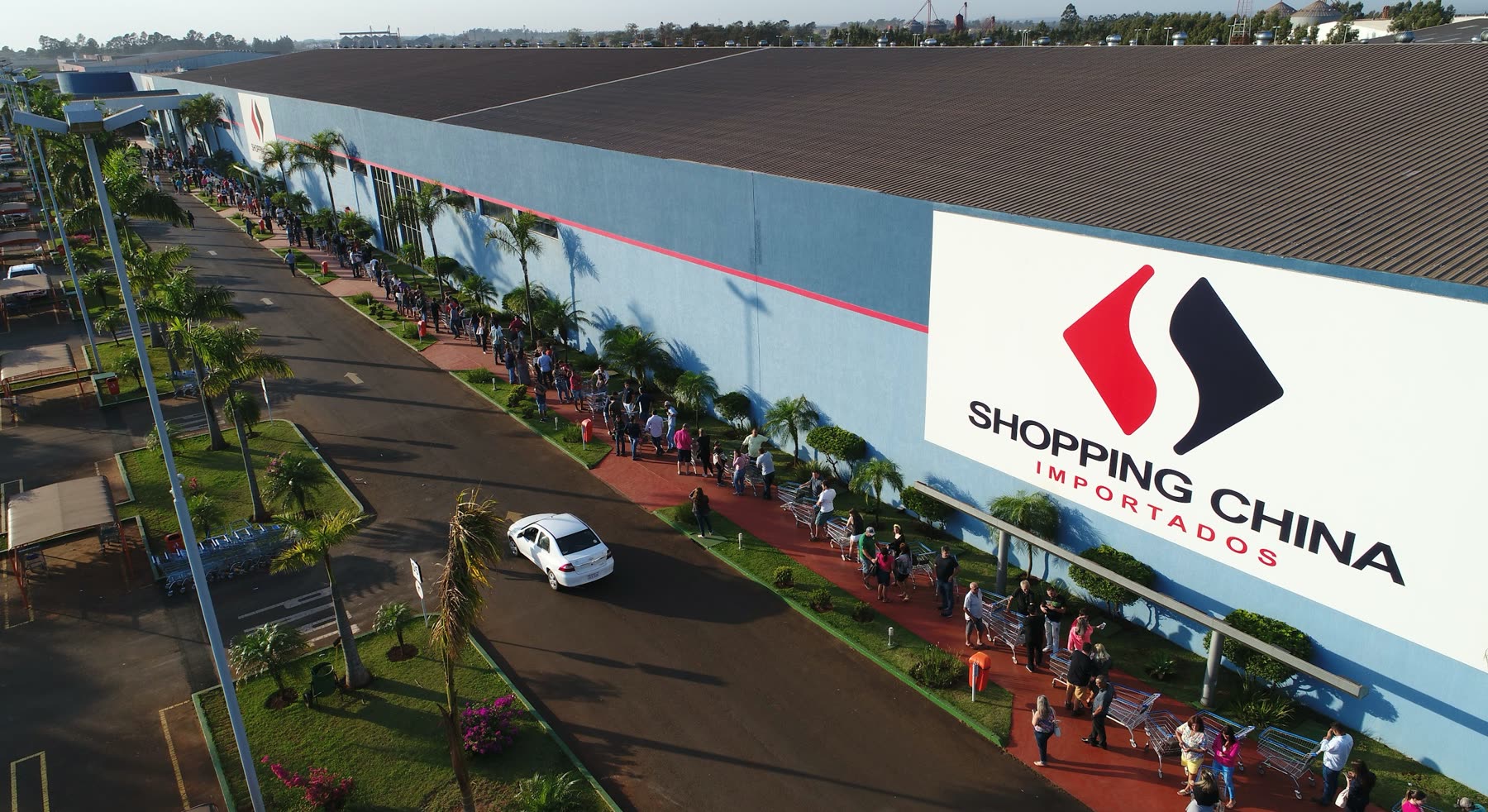Vista aérea de un edificio alargado con el letrero Shopping China Importados y una fila de personas a lo largo de la vereda